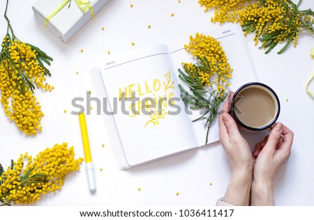Spring flat lay with yellow flowers, notepad . Woman\'s hand are holding a cup of coffee. Hello spring concept top view composition