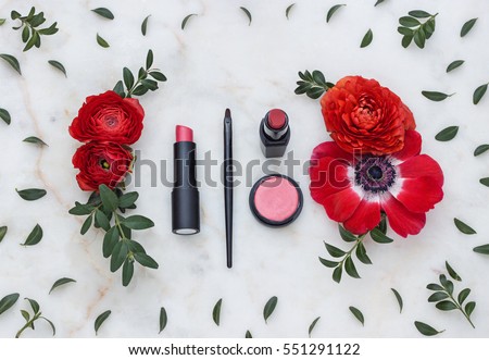 Beauty flat lay with decorative cosmetics and red flowers on the marble background. Top view