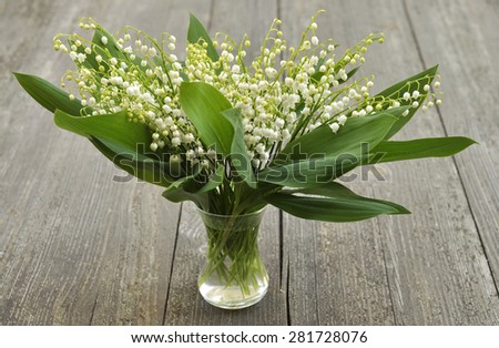 Bouquet of lilies of the valley in glass vase on wooden background