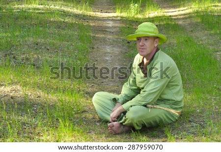 An elderly man in a green hat and green clothes sitting on the grass