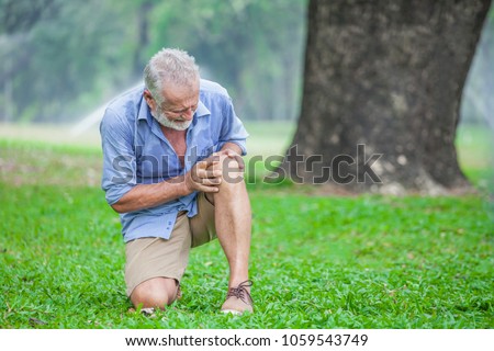 Senior man sitting or flop falling  in autumn park and having knee pain. kneel Arthritis pain concept.