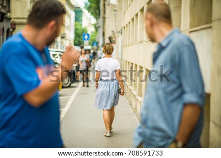 Two men on a street shouting rude words to a girl walking by. Catcalling, verbal sexual harassment concept.