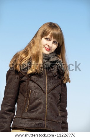Portrait of a pretty blonde girl with muffler and short fur coat on sky background