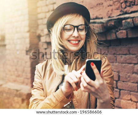 City lifestyle stylish hipster girl using a phone texting on smartphone app in a street