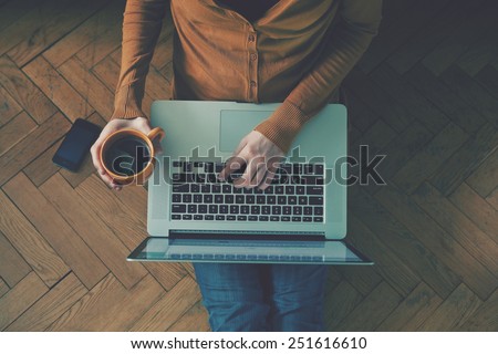 Laptop and coffee cup in girl\'s hands sitting on a wooden floor
