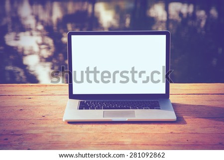 laptop with blank screen for copyspace on wooden boards table on natural summer water background