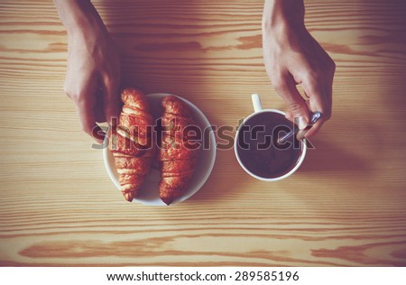 Hands holding cup of coffee and croissants. View from above