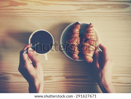 Hands holding cup of coffee and croissants. View from above