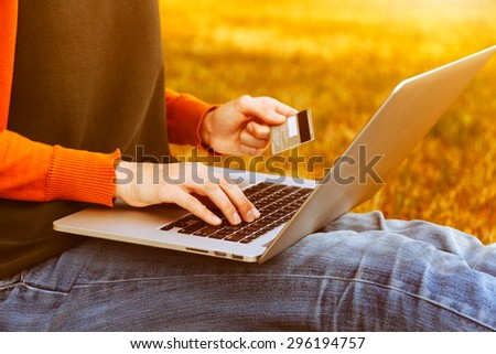 Hands holding credit card and using laptop on natural summer background. Online shopping