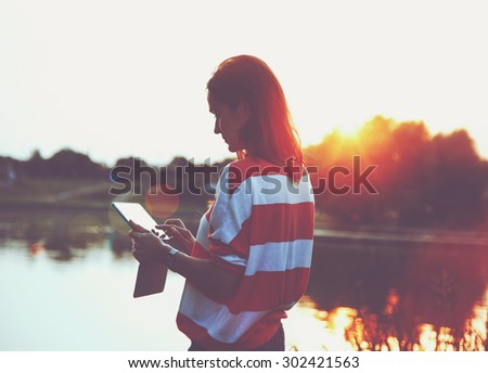 girl holding digital tablet pc at lake shore in sunrise light