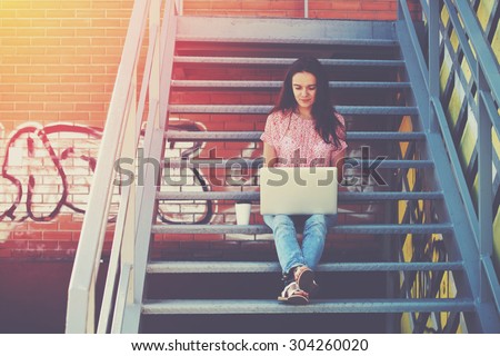 Pretty girl working with laptop sitting on stairs of stairway
