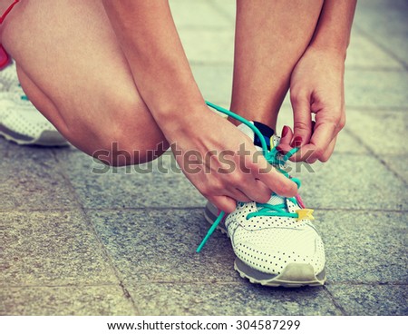 Girl getting ready for training and jogging at park tying shoes laces. Close-up