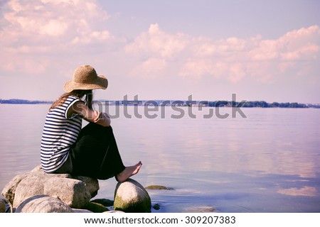 stylish woman alone sitting on stone coast and looking at sea