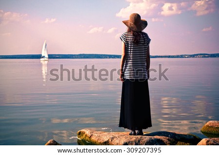 woman standing alone at sea coast and looking on ship