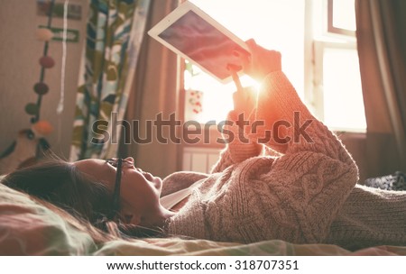 woman lying in bed with digital tablet touching with finger in morning sunlight