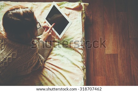 Woman lying in bed with digital tablet touching with finger. View from above