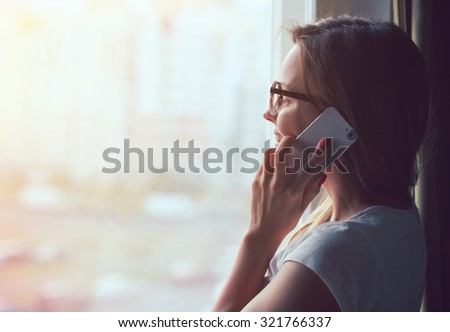 pretty woman talking on phone near window at home in morning sunlight