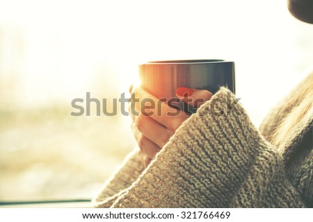 hands holding hot cup of coffee or tea in morning sunlight