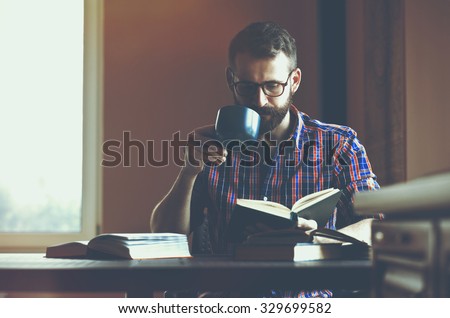 concentrated bearded man reading books and drinking coffee or tea