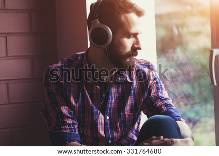 stylish bearded man  in headphones listening to music near window with reflection