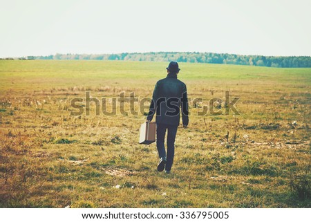 man going with suitcase in field. Concept freedom, loneliness or traveling concept