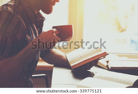 bearded man reading book with coffee or tea