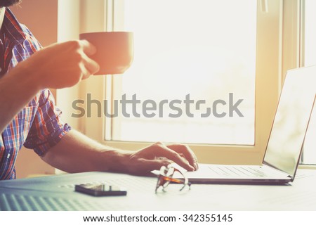 male hand working with laptop and cup of tea or coffee
