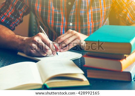 male hand writing with pen near books