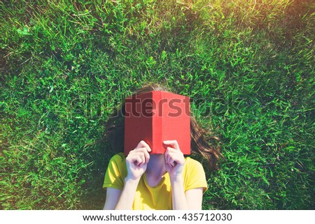 girl reading book lying in warm summer grass. view from above