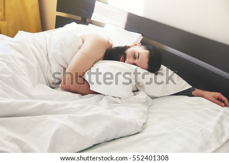 Bearded man lying in bed and dreaming in morning sunrise light