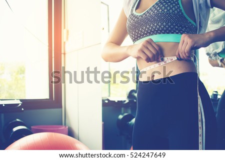 woman checking success of weight loss program with measuring tape at gym.