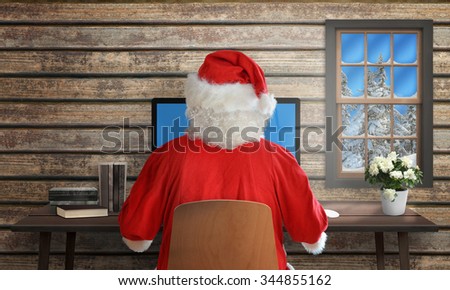 Santa Claus sitting at the computer on desk. Cottage interior with window.