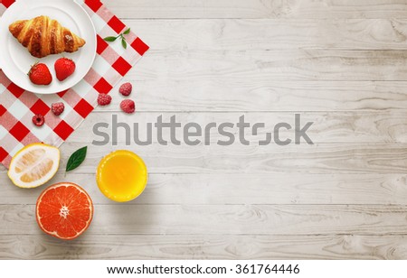 Fruit breakfast with free space on wooden table. Croissant, orange, strawberries, raspberries, lemon, juice, with top view.