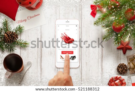 Woman buy shoes online with mobile phone during Christmas time. Table with Christmas decorations. Christmas tree and gifts beside.