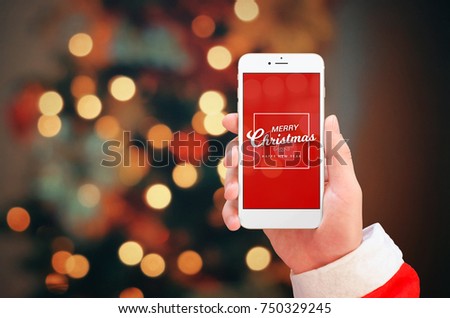 White mobile phone in Santa Claus hand close up. Merry Christmas greeting on phone display. Christmas bokeh lights in background.