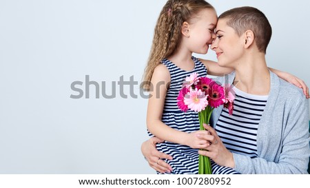Happy Mother's Day, Women's day or Birthday background. Cute little girl giving mom bouquet of pink gerbera daisies. Loving mother and daughter smiling and hugging.
