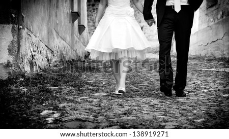 horizontal black & white image of bride & groom holding hands walking towards the camera
