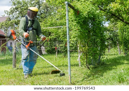 Male worker with power tool string lawn trimmer mower cutting grass. Health and safety concept.