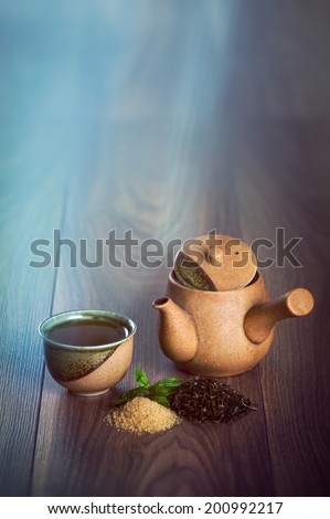 Ceramic teapot, cup of black tea with mint leaves and brown sugar on wooden table with copy space