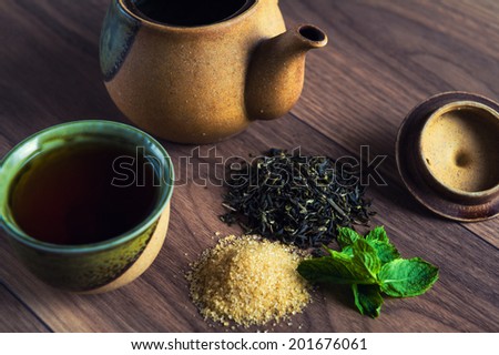 Ceramic teapot, cup of black tea with mint leaves and brown sugar on wooden table