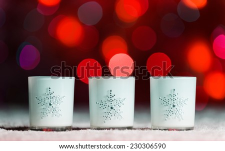 Set of 3 candles standing in snow with defocussed fairy lights, red bokeh in the background, Festive Christmas background with copyspace