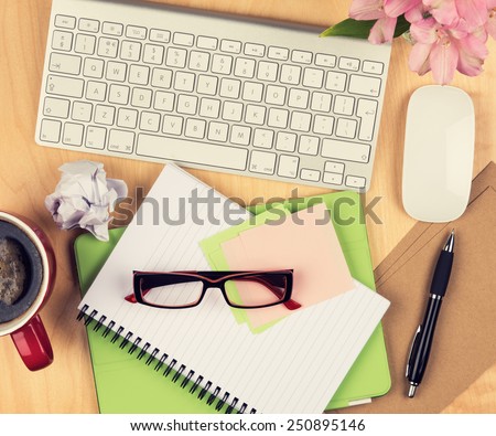 Messy office table with notepad, computer, reading glasses and coffee cup. View from above with copy space