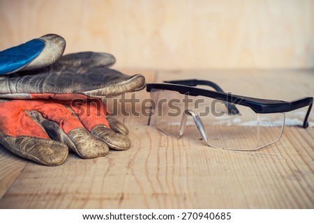 Old used safety glasses and gloves on wooden background
