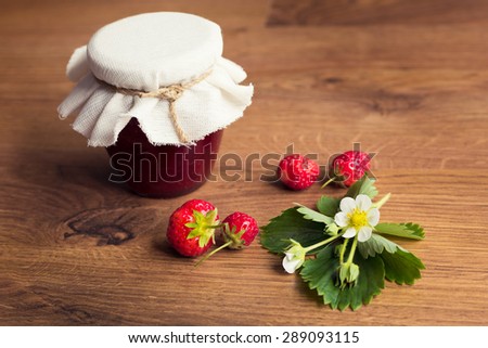 Homemade strawberry jam (marmalade) in jars on wooden background.
