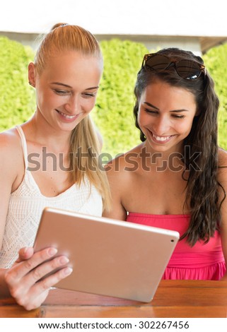 holidays, tourism, technology and internet - two beautiful girls looking at tablet pc computer in cafe outside