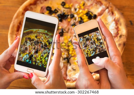 Female friends using smartphones to take photos of their pizza