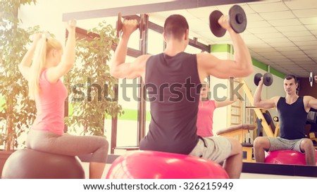 Young couple training in gym with dumbbells in front of a mirror sitting on fitballs