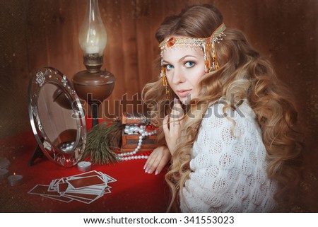 Young beautiful girl sits near a fortune teller desk with a lamp and candles. Card reading. Divination