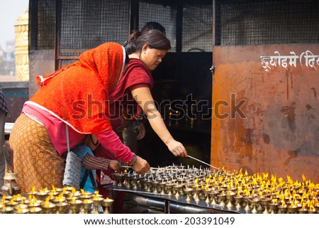 KATHMANDU, NEPAL - MARCH 28: An unidentified tibetan woman lights incense butter candles in honor of Losar holiday on March 28, 2014 in Boudhanath, Kathmandu Valley, Nepal