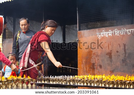 KATHMANDU, NEPAL - MARCH 28: An unidentified tibetan woman lights incense butter candles in honor of Losar holiday on March 28, 2014 in Boudhanath, Kathmandu Valley, Nepal